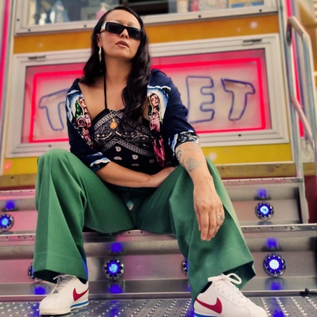 DJ Asia Knox auf der Treppe eines sehr bunten Kirmes Fahrgeschäfts
