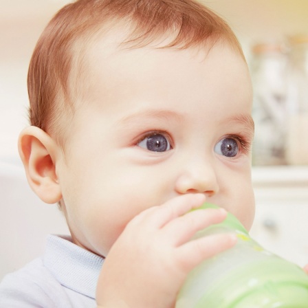 Ein Baby mit blauen Augen trinkt aus einer Trinkflasche
