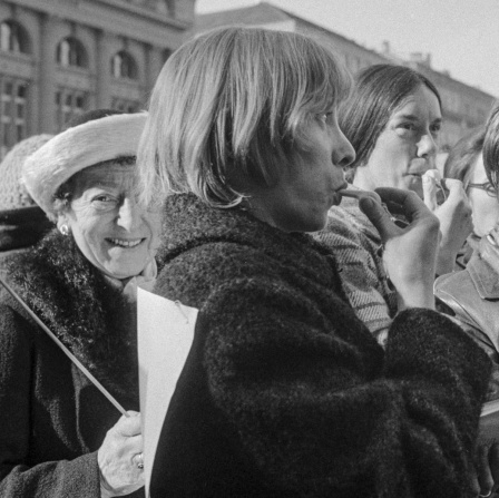 Auf einer Demonstration in Bern stehen Frauen und Männer zusammen, es werden Plakate gehalten, Frauen machen Lärm mit Trillerpfeifen.