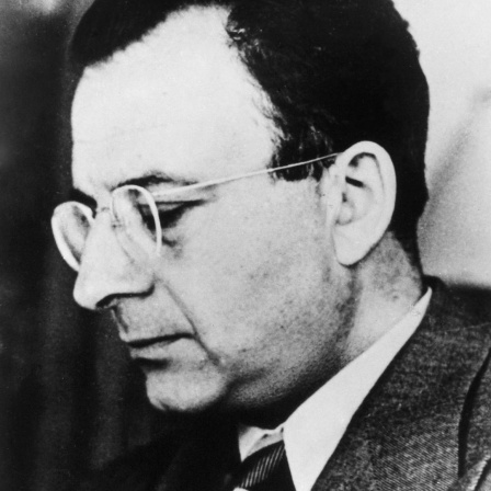Schwarz-weiße Seitenaufnahme von Erich Fromm mit Brille und im Anzug.