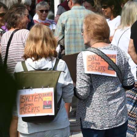 "Sylterinnen gegen Rechts!“ steht auf Plakaten, die zwei Frauen bei einer Mahnwache auf Sylt auf ihre Rücken geheftet haben.