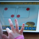 Kinderfinger tippen auf einem Tablet auf dem spielerisch eine Rechenaufgabe dargestellt ist.