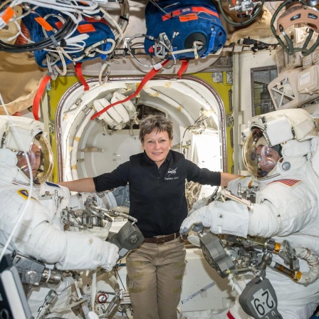 US-Astronautin Peggy Whitson eingerahmt von zwei männlichen Kollegen in Raumanzügen auf der Internationalen Raumstation.