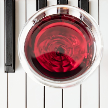 Ein Glas Rotwein auf den Tsten eines Klaviers.