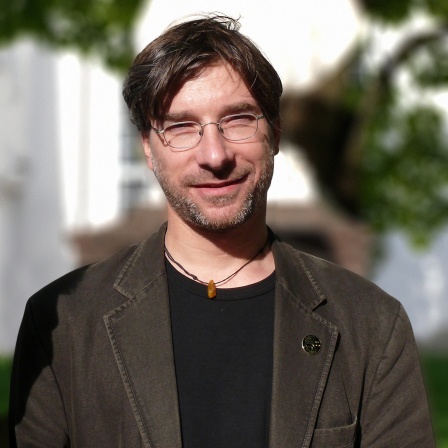 Ein Mann mit Brille und dunklen Haaren schaut in die Kamera