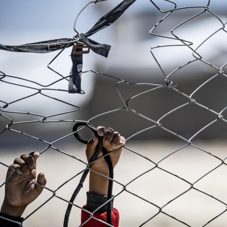 Das Bild zeigt die Hände eines Kindes, das an einem Zaun im Lager im Nordosten Syriens versucht ein Band zu befestigen.