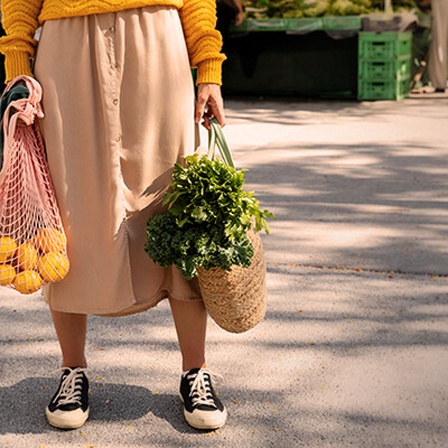 Eine Frau hält Netze mit Obst- und Gemüseeinkäufen in den Händen.