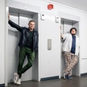 Devid Striesow und Axel Rahnisch stehen jeweils vor einer Fahrstuhltür.