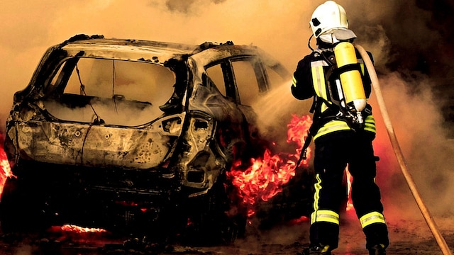 Ein Feuerwehrmann löscht ein brennendes Auto mit dem Feuerwehrschlauch.