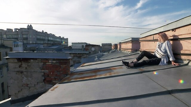 Eine junge Frau sitzt auf einem Stadtdach in Stankt Petersburg und schaut in die Ferne.