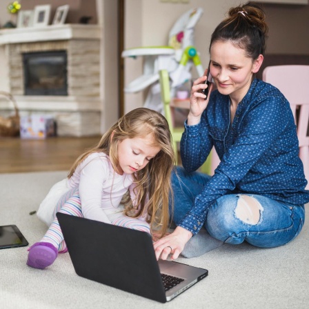 Frau, die mit ihrer Tochter zusammensitzt und mit dem Handy spricht (Bild: picture alliance / imageBROKER / Oleksandr Latkun)