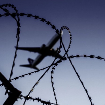 Ein Flugzeug fliegt hinter Stacheldraht (Bild: picture alliance/Robert Schlesinger)