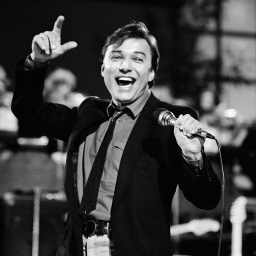 Der Sänger Karel Gott, bekannt für Lieder wie &#034;Die Biene Maja&#034;, tritt in einer Fernsehshow auf und singt lachelnd (Schwarz-Weiß-Foto).