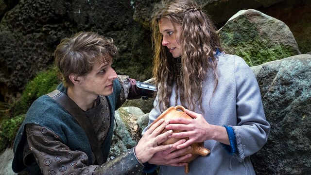 Szenenbild - Der süße Brei - Jolanthe (Svenja Jung) und Veit von Hammerlitz (Merlin Rose) stehen auf einer Waldlichtung dicht bei einander, umfassen den magischen Topf und blicken sich tief in die Augen.