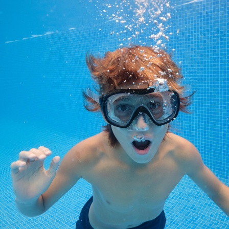 Ein Junge mit Taucherbrille unter Wasser im Pool