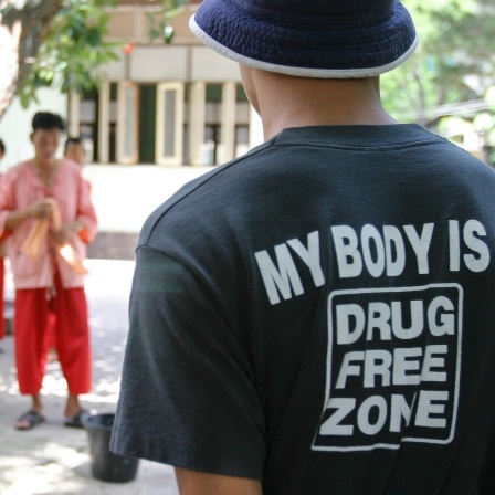 Buddhistisches Drogenentzugskloster Wat Thamkrabok in Thailand: Auf dem Rücken des T-Shirts eines Studenten steht die Aufschrift "my body is a drugfree zone",; im Hintergrund in roten Gewändern sind Mönche des Klosters zu sehen.