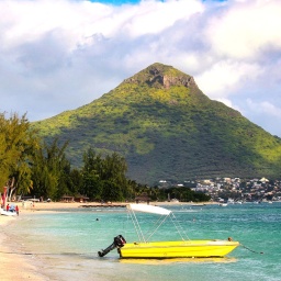 Ein gelbes Boot mit kleinem Außenmotor liegt am Strand von Mauritius, dahinter ist ein Hügel zu erkennen, auch Palmen am weißen Strand