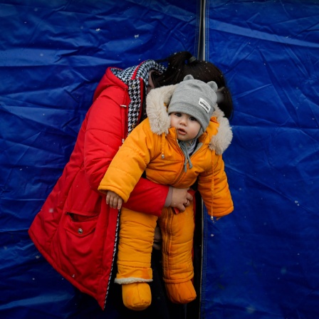 Vor einem Zelt in einem Flüchlingslager hält eine ukrainische Frau ihr Kind im Arm