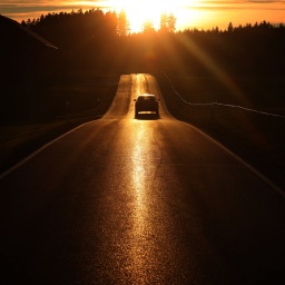 Ein Auto fährt auf einer Landstraße der tief stehenden Sonne entgegen.