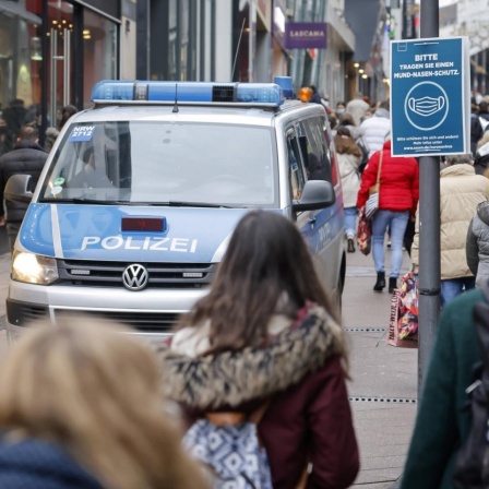 Passanten mit Schutzmasken beim Einkauf im Zentrum der Stadt Essen, links ein Polizeifahrzeug. 