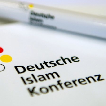 Ein Kugelschreiber liegt auf dem Logo der Deutschen Islam Konferenz 