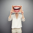 Frau hält sich Foto eines lachenden Mundes vor das Gesicht