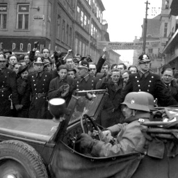 Einheiten der deutschen Wehrmacht ziehen am 15. März 1939 in Prag ein. Am Straßenrand stehen Einwohner der Stadt, die den Einmarsch mit geballten Fäusten quittieren.