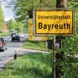 An einer Straße steht ein Ortsschild von Bayreuth. 