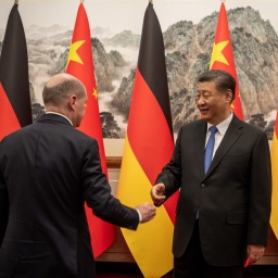 Scholz geht auf Xi Jinping zu, der vor deutschen und chinesischen Flaggen steht