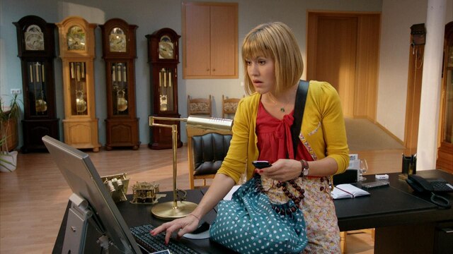 Eine Frau steht an einem Schreibtisch vor einem Laptop. Im Hintergrund stehen Standuhren.