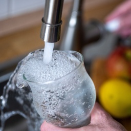 Trinkwasser läuft aus dem Wasserhahn in einer Küche in ein Glas.