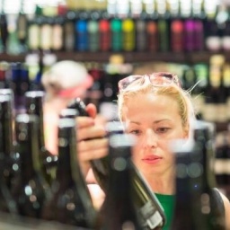Frau schaut sich im Supermarkt eine Flasche Wein an.