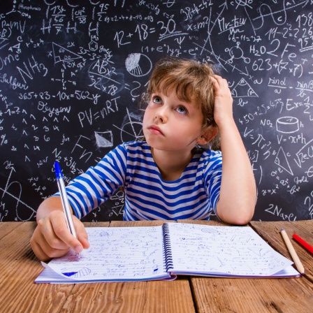 Junge sitzt vor Schultafel mit vielen Matheaufgaben und denkt nach: Schlecht in Mathe - oft liegt das an schlechtem Unterricht, nicht an mangelndem Talent. Gute Mathe-Didaktik setzt auf Verstehen statt auswendig lernen und begeistert für das Fach.
