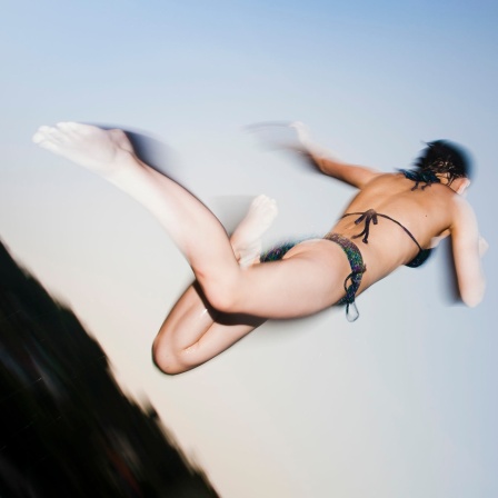 Momentaufnahme von einer Jugendlichen die in der Luft schwebt, als sie von einem Sprungbrett ins Wasser gesprungen ist.