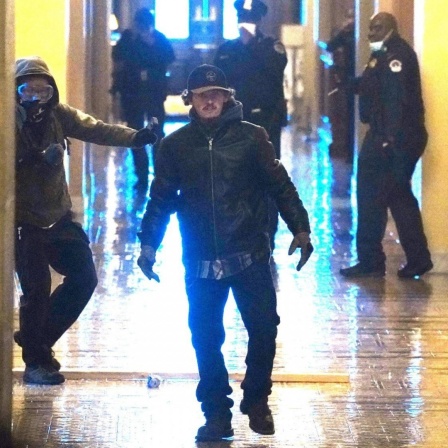 Zwei Protestler, die ins Kapitol eingedrungen sind, laufen auf die Kamera zu. Im Hintergrund stehen Polizisten.