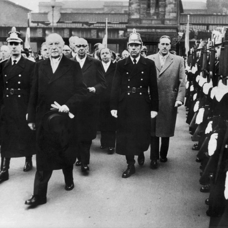Nach seiner Ankunft in Saarbrücken schreitet Bundeskanzler Konrad Adenauer (2.v.l.) auf dem Bahnhofsvorplatz die Front der Polizeihundertschaft ab, hinter Adenauer der Ministerpräsident der Saarregierung, Hubert Ney.