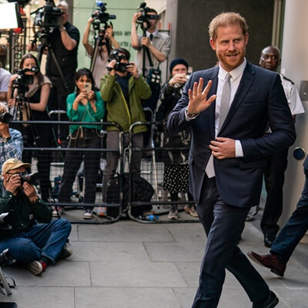 Prinz Harry verlässt winkend ein Gerichtsgebäude, vor ihm warten Kameras und Journalisten