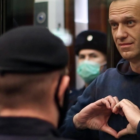 Alexei Nawalny formt mit seinen Händen ein Herz, während er bewacht hinter einer Glasscheibe seht.