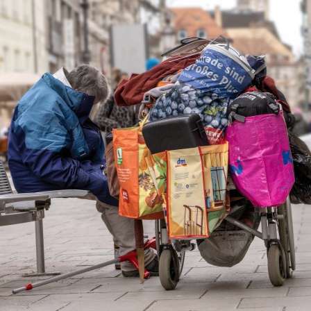 Obdachloser mit seinen Habseligkeiten in der Innenstadt auf einer Bank.