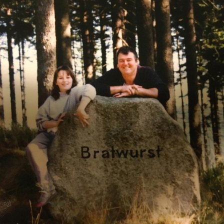 Eine Frau und ein Mann stehen hinter einem großen Stein, auf dem "Bratwurst" steht.