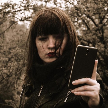 Eine Frau steht im Wald und schaut auf ihr Smartphone.