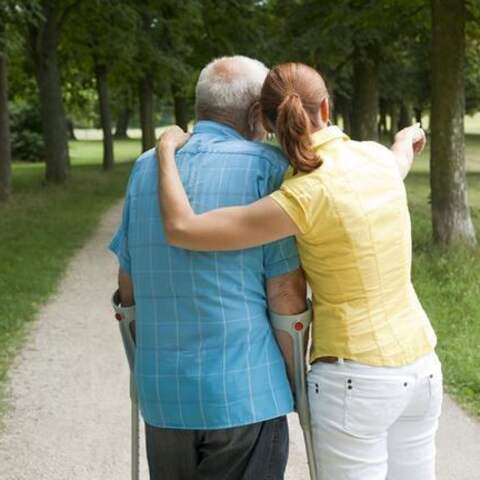 Frau und älterer Mann mit Krücken machen einen Spaziergang im Park