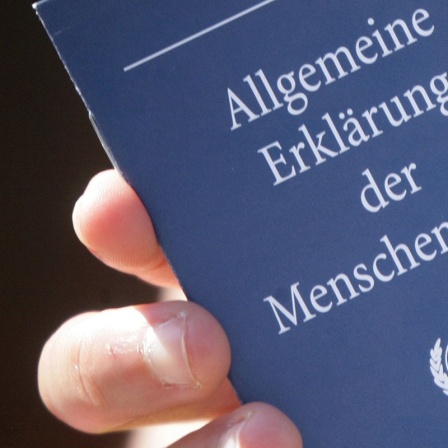 Eine Hand hält ein kleines Heft mit dem Titel "Allgemeine Erklärung der Menschenrechte hoch".