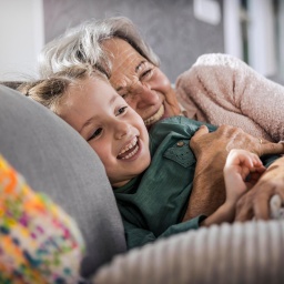 Grossmutter hat Spass mit Enkelin auf Couch im sonnigen Wohnzimmer || Modellfreigabe vorhanden