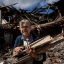 Eine ältere Frau räumt die Trümmer eines im Krieg zerstörten Hauses in der Ukraine auf