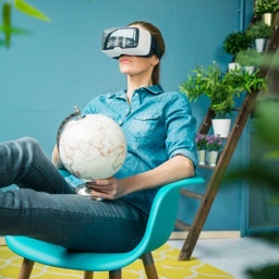 Frau sitzt in ihrem mit Pflanzen geschmückten Haus, hält einen Globus in der Hand und trägt eine VR-Brille.