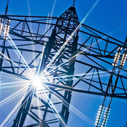 Ein Strommast mit Sonnenstrahlen und blauem Himmel im Hintergrund.