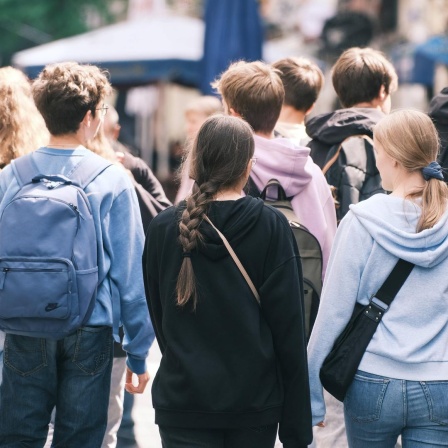 Mehrere Jugendliche laufen auf einer Straße entlang, sie sind von hinten zu sehen. 