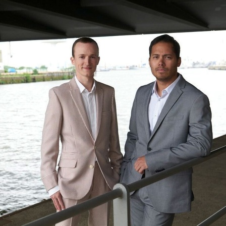 Zwei junge Männer stehen unter einer Brücke an einem Fluss.