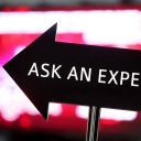 Ein Pfeil-Schild, auf dem "Ask an Expert" steht, vor dem Hintergrund eines roten Computerbildschirms